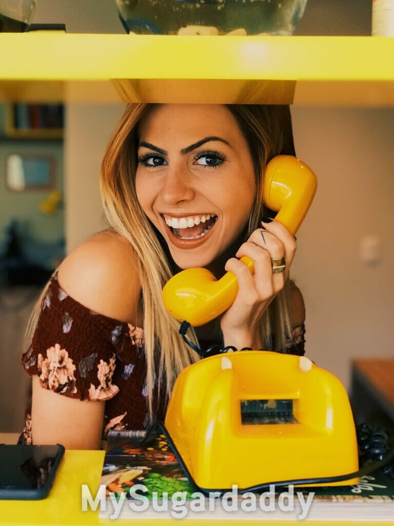 conquistare uno sugar daddy - ragazza bionda solare che usa un telefono antico giallo e sorride